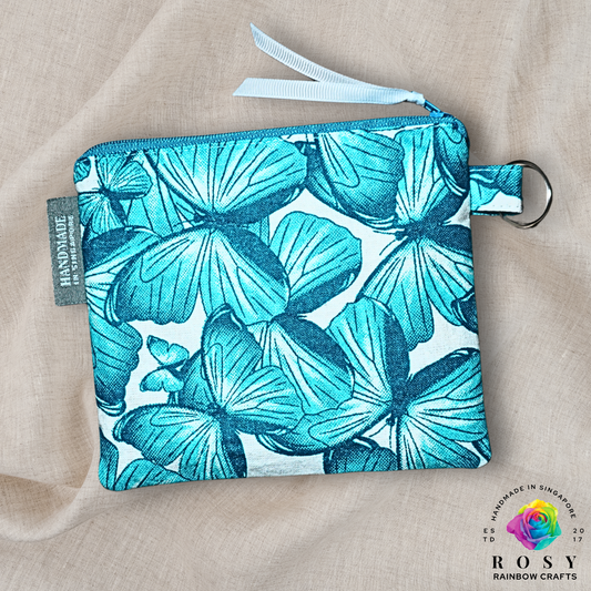 Fabric pouch with turquoise butterfly pattern on beige fabric, featuring Rosy Rainbow Crafts branding.