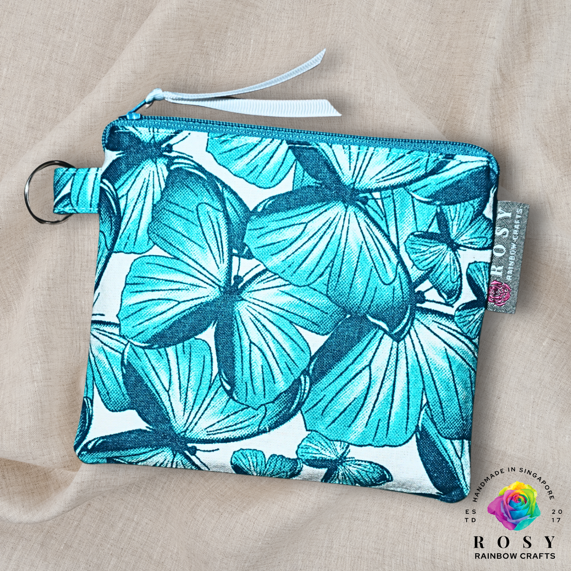 Fabric pouch with turquoise butterfly pattern on a beige background, featuring the Rosy Rainbow Crafts brand.